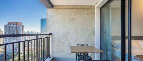 Un balcon avec une table et des chaises, une vue sur le paysage urbain et une grande fenêtre.