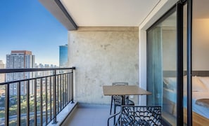 A balcony with a table and chairs, a bed, and a city view.
