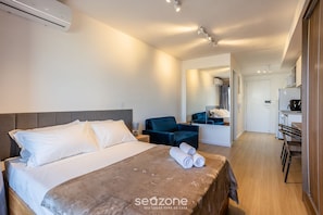 A hotel room with a bed, a desk, a chair, and a kitchenette.