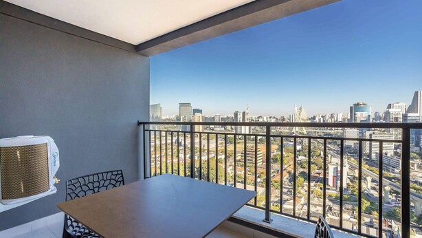 A balcony with a table and chairs, overlooking a cityscape with modern buildings and a bridge. - Apt w/ Balcony, Minutes From the Subway Ctb2405 (São Paulo)