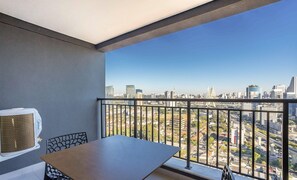 Un balcón con mesa y sillas, con vista a un paisaje urbano con edificios modernos y un puente.