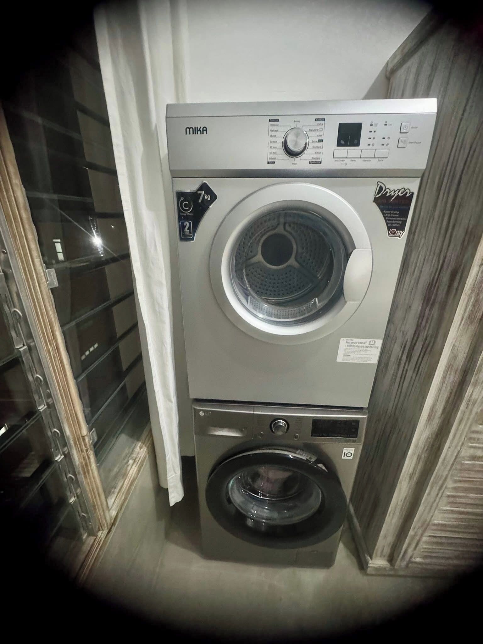 A MIKA front-loading washing machine with a control panel, a smaller front-loading machine below it, and a glass door with a metal handle.