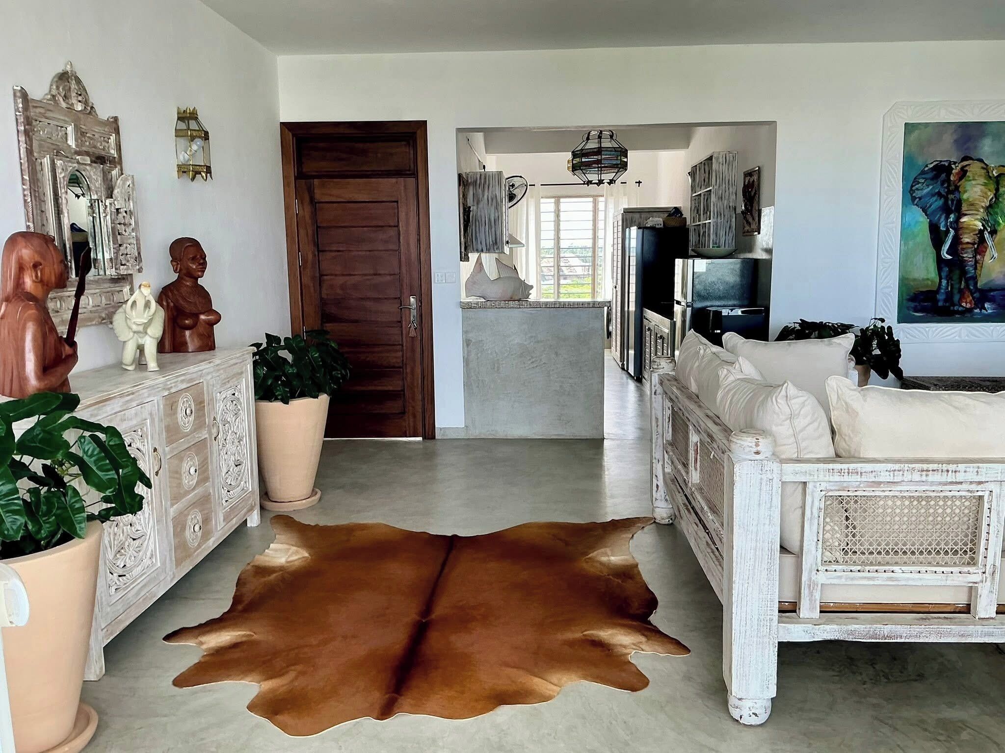 Amplia sala de estar con alfombra de cuero, sofá blanco y mueble de madera con objetos decorativos.