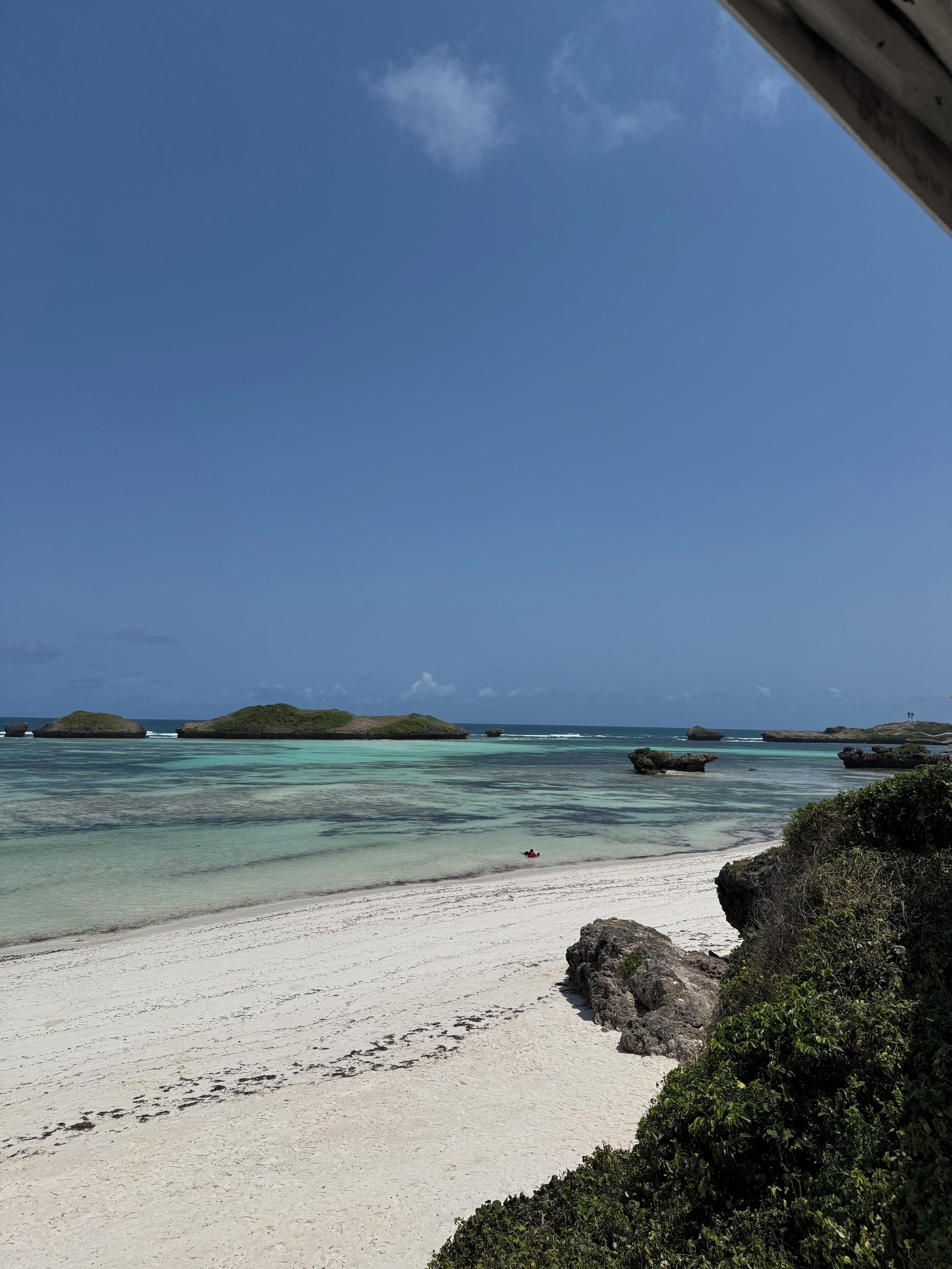 A beach with clear turquoise waters, white sand, and rocky outcrops.