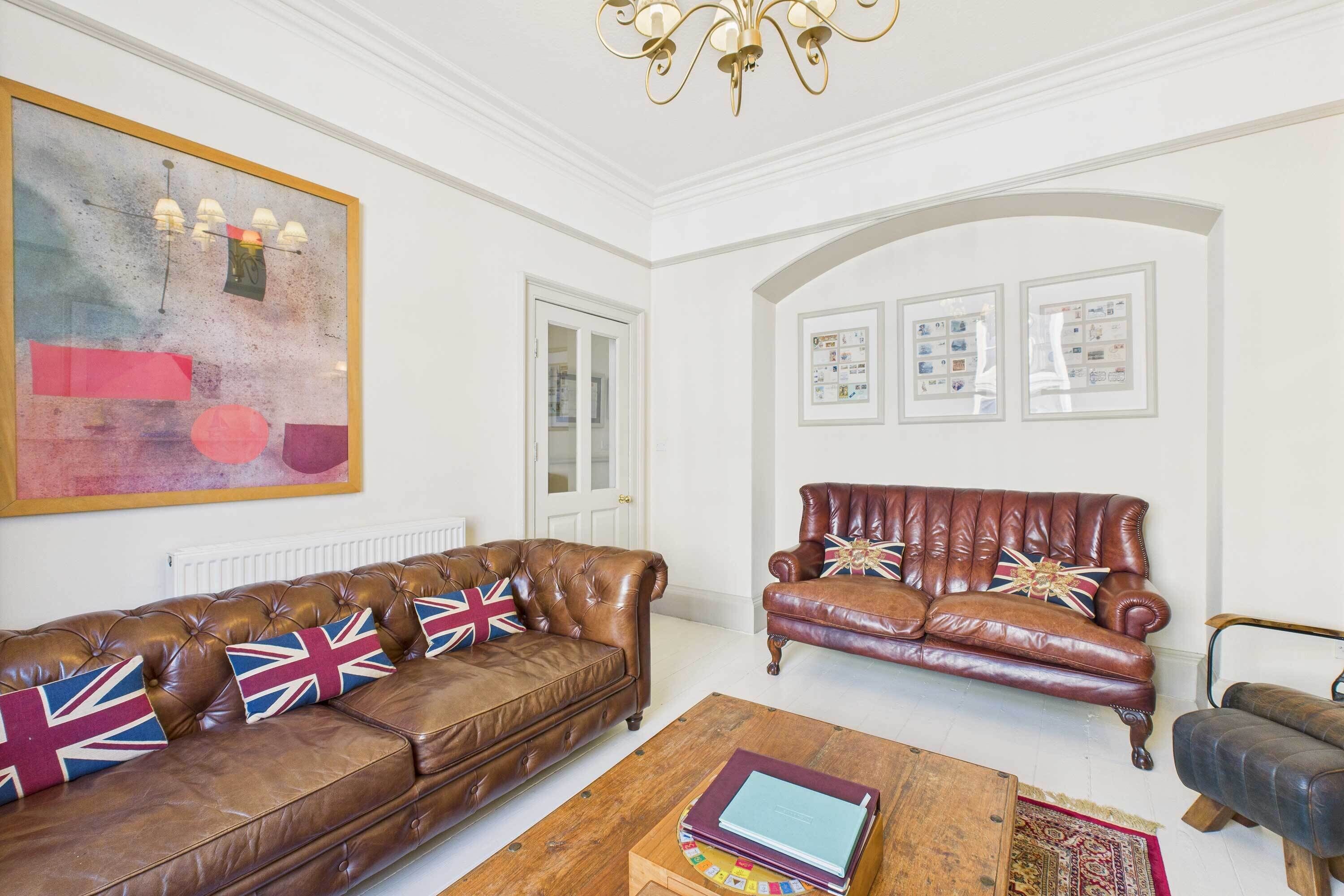 A spacious living room with leather sofas, a wooden coffee table, and a chandelier.