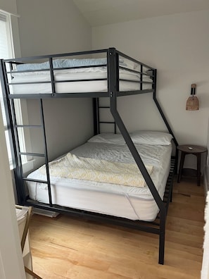 Una cama litera con escalera, una mesita pequeña y una lámpara colgante en una habitación con piso de madera.