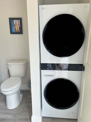 A compact washer and dryer unit in a bathroom with a toilet and a framed picture on the wall. - Charming, renovated 2-bedroom cottage in Old Orchard 100 yds to the beach (Old Orchard Beach)