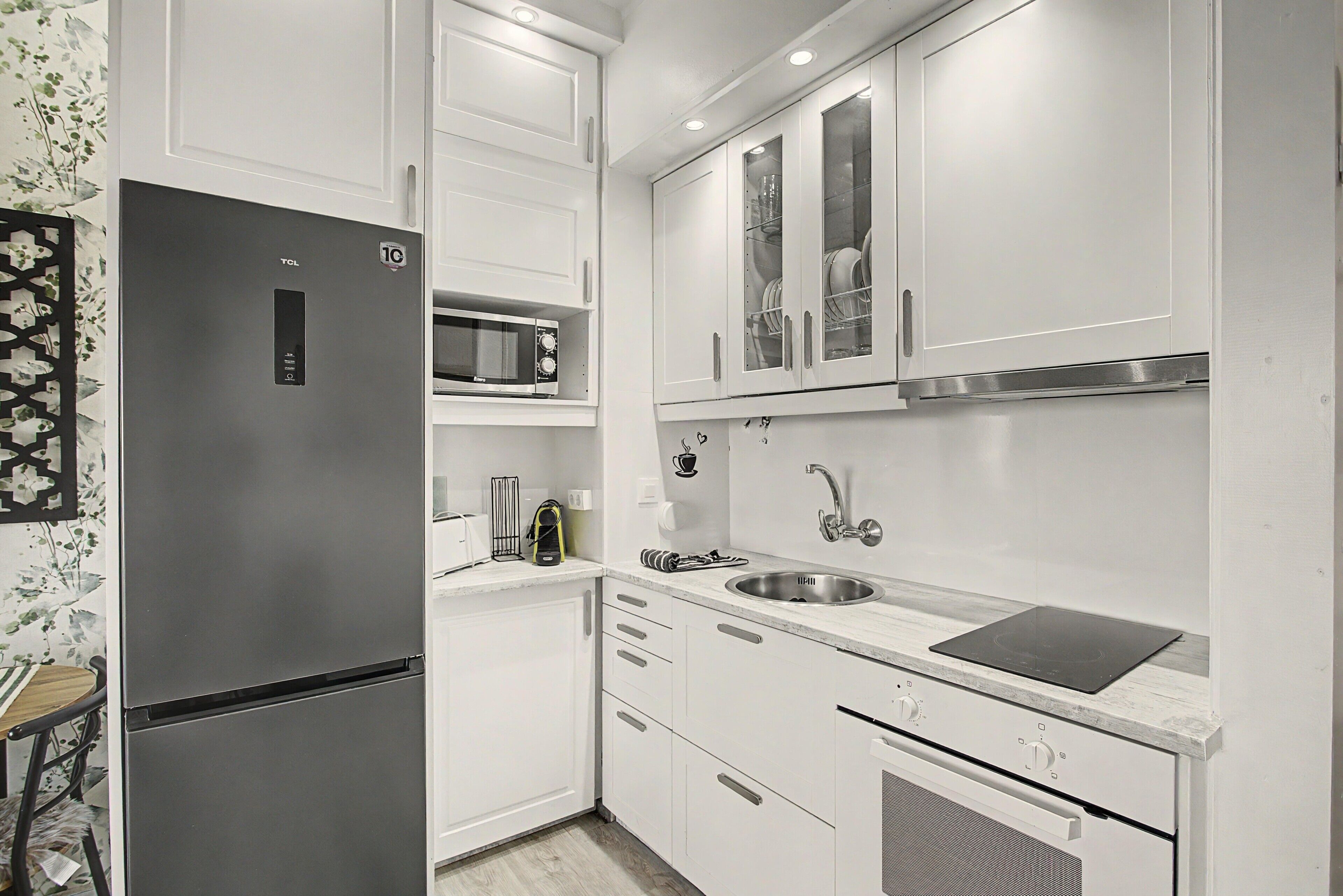 Una cocina moderna con armarios blancos, microondas integrado, pileta de acero inoxidable y cocina por inducción negra.