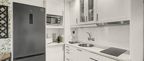 Una cocina moderna con armarios blancos, microondas integrado, pileta de acero inoxidable y cocina por inducción negra.