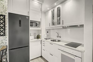 A modern kitchen with white cabinetry, a built-in microwave, a stainless steel sink, and a black induction cooktop.