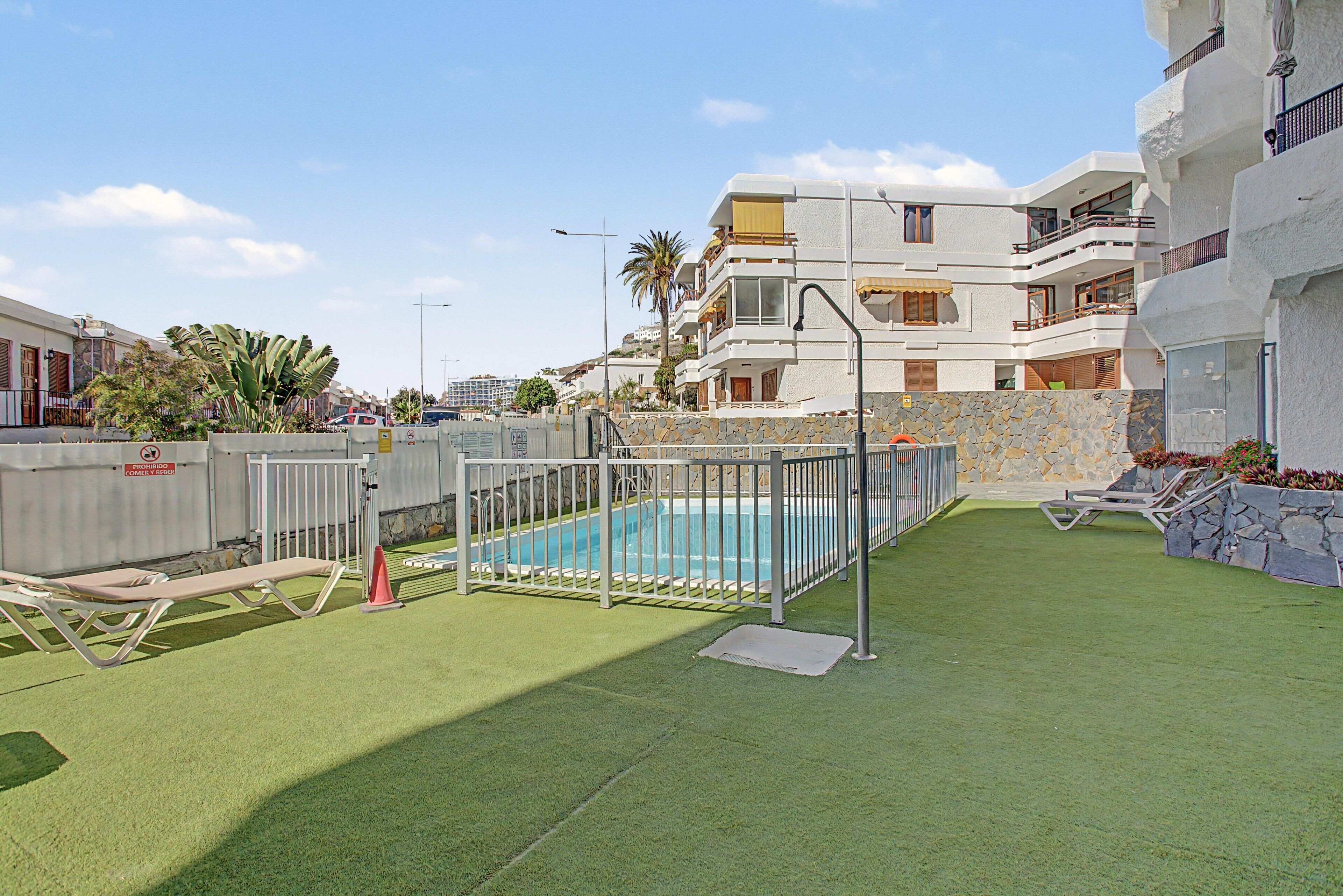 Un quartier résidentiel doté d’une piscine entourée d’une clôture en métal, d’une pelouse verdoyante et d’un mur en pierre.