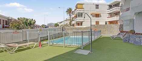 A residential area with a swimming pool surrounded by a metal fence, a grassy lawn, and a stone wall.