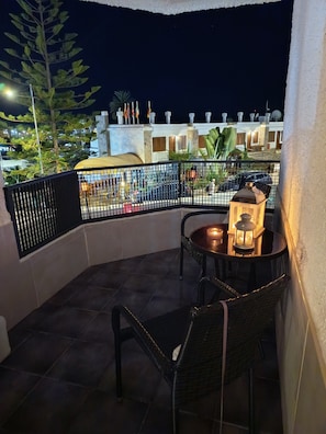 A balcony with a table and chairs, a lantern, and a view of buildings at night.
