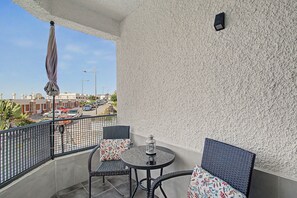 A balcony with a round table and two chairs, a small lantern, and a view of a street with cars and buildings. - Apartment Two Minutes from the Beach. Puerto Rico (Mogán)