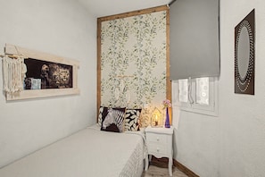 A bedroom with a bed, a nightstand, a mirror, and a wall with a floral tapestry. - Apartment Two Minutes from the Beach. Puerto Rico (Mogán)