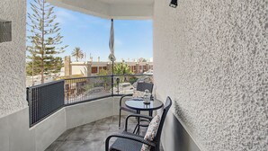 Un balcon avec une table et des chaises, un luminaire suspendu, et une vue sur les bâtiments environnants et les palmiers.