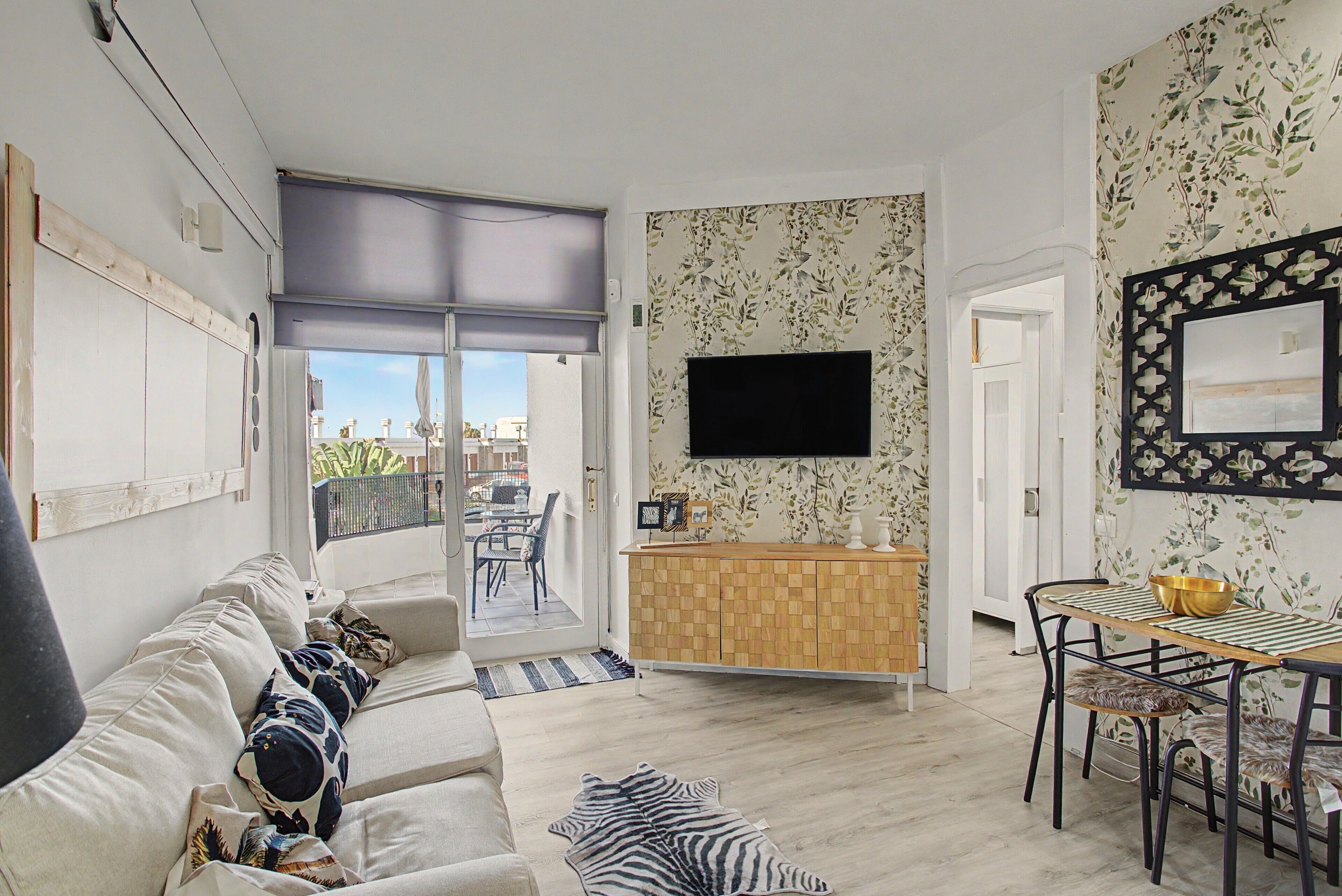 Ein Wohnzimmer mit einer Couch, einem Esstisch mit Stühlen, einem an der Wand befestigten Fernseher und einem Balkon mit Blick.