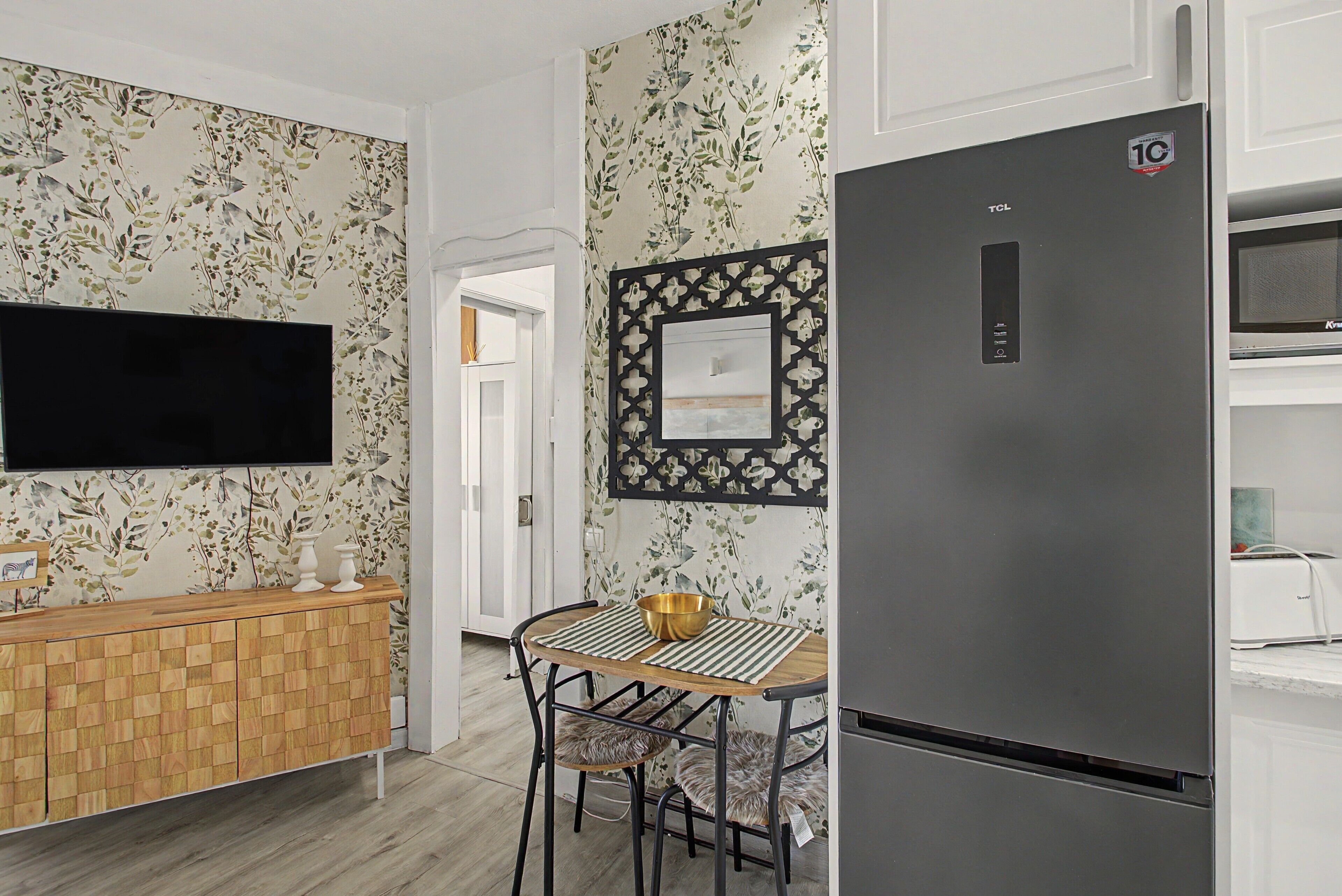 Una cocina moderna con un armario de madera, un refrigerador negro, una mesa de comedor con un mantel a rayas y un adorno en la pared.