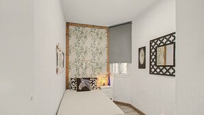 Une chambre à coucher comprenant un lit, une commode, un miroir et un mur recouvert d’un papier peint à motifs floraux.
