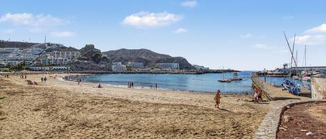 A beach with a rocky outcrop in the background, a clear sky, and a calm sea.