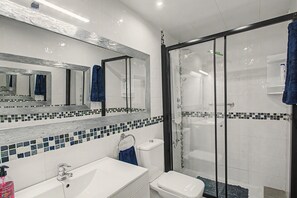 A bathroom with a white sink, a toilet, a glass-enclosed shower, and a mirror above the sink. - Apartment Two Minutes from the Beach. Puerto Rico (Mogán)