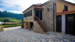 A stone building with a tiled entrance, a staircase, and a view of green fields. - Villa 'Casa Dos Leões' with Mountain View, Private Pool and Wi-Fi (Ponte de Lima)