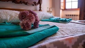 A bed with a teal blanket, a decorative headboard, and a window with natural light. - Villa 'Casa Dos Leões' with Mountain View, Private Pool and Wi-Fi (Ponte de Lima)
