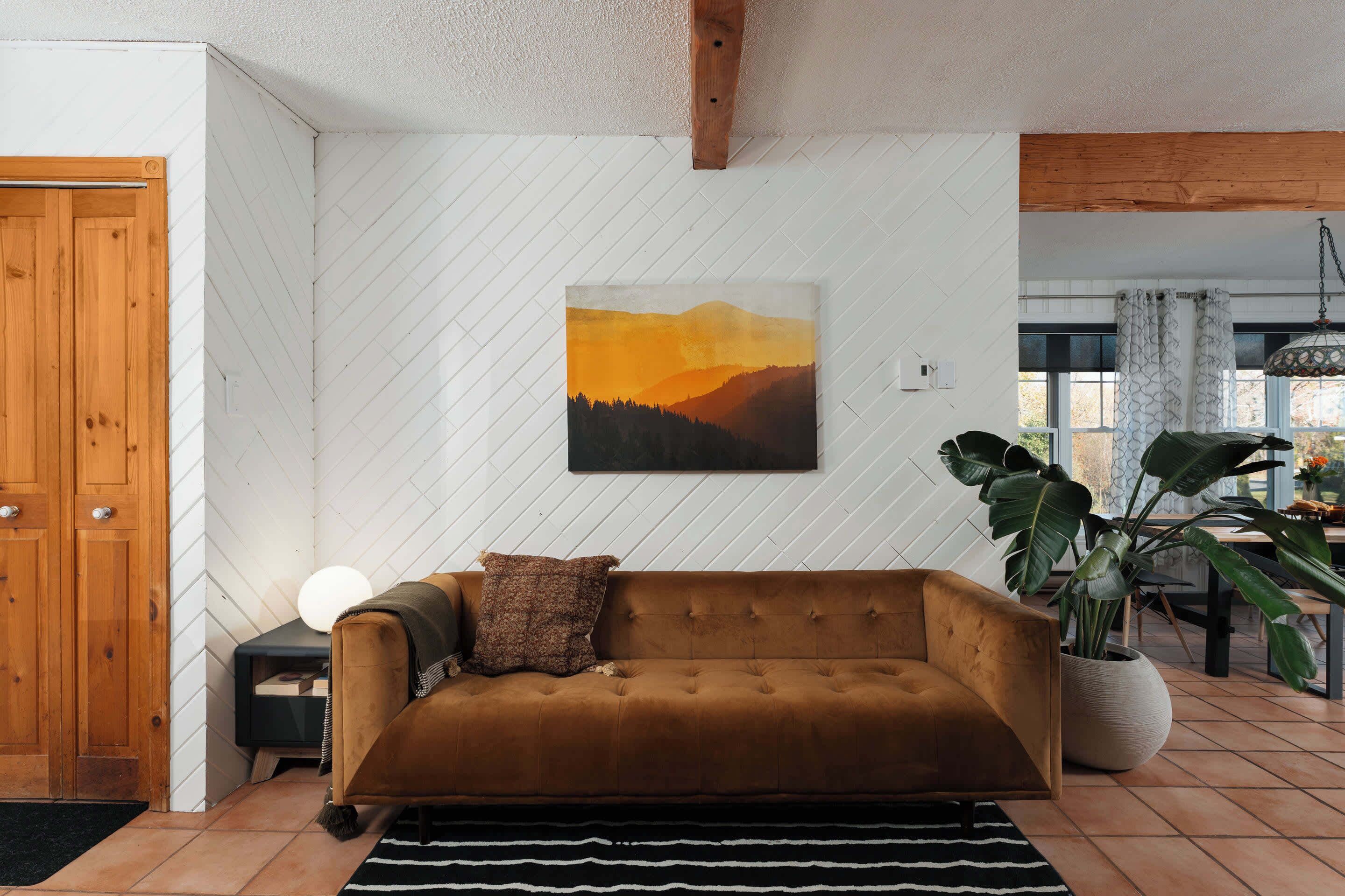 Un salon avec un canapé marron, un tableau représentant un coucher de soleil, une plante en pot et une porte en bois.