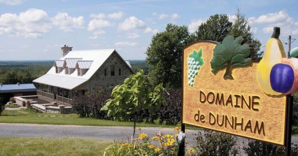 Señal de Domaine de Dunham, con un rústico edificio de piedra al fondo.