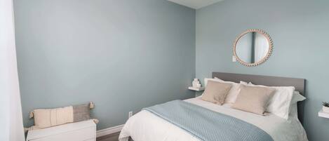 Quarto com cama, mesas de cabeceira, ventilador de teto, espelho redondo e parede azul clara.