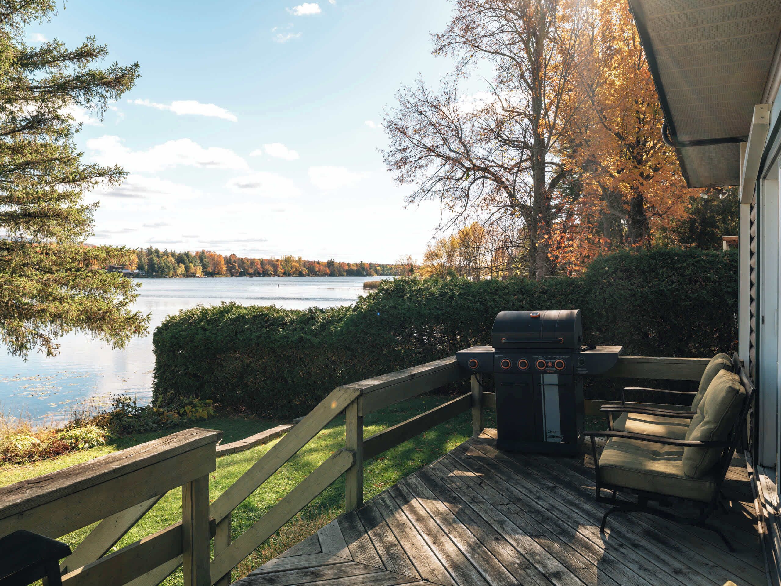 A deck with a grill, a chair, and a view of a lake.