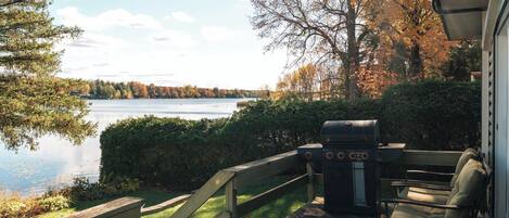 A deck with a grill, a chair, and a view of a lake.