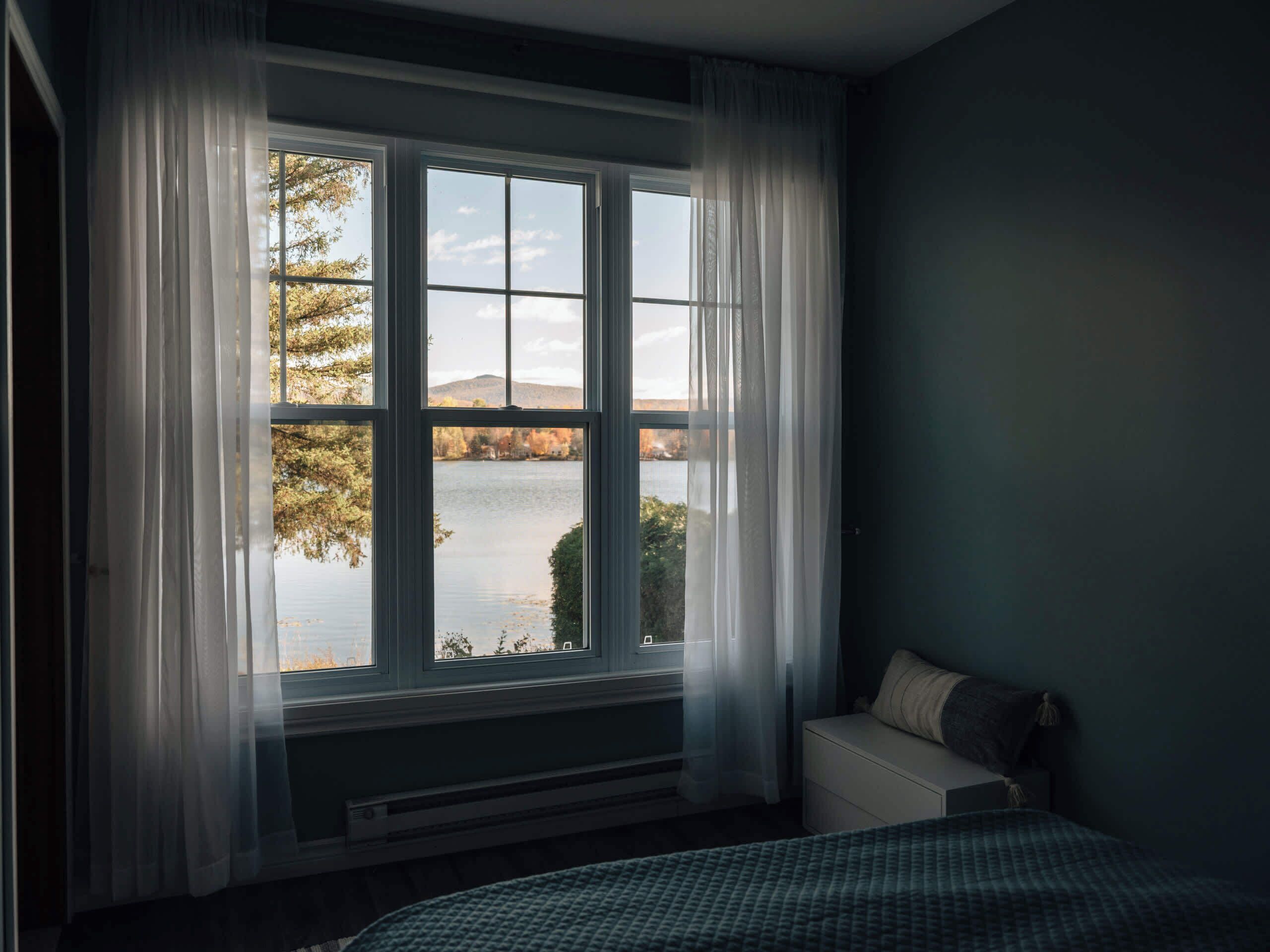 A bedroom with a large window, a bed, and a nightstand.