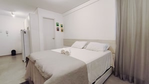 A hotel room with a bed, a door, a trash bin, and a wall-mounted phone.