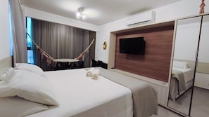 Una habitación de hotel con cama, televisión montada en la pared, espejo y ventana con cortinas.