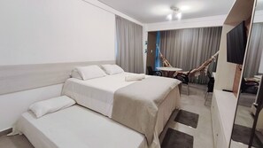 A hotel room with a bed, a sofa, a desk with a chair, a hammock, and a television.