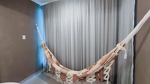 A hammock in a room with a grey curtain and a light switch on the wall. - Villa Del Porto - Porto de Galinhas (Ipojuca)
