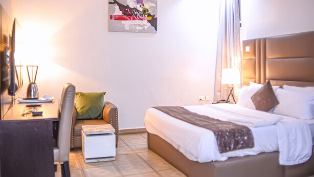 Ein Hotelzimmer mit einem Bett, einem Schreibtisch mit Stuhl, einem kleinen Tisch, einer Lampe und einer Wandklimaanlage.