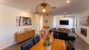 A modern living room with a wooden dining table, black leather sofa, and a TV mounted on the wall. - Grange Retreat - Beach, BBQ (Grange)