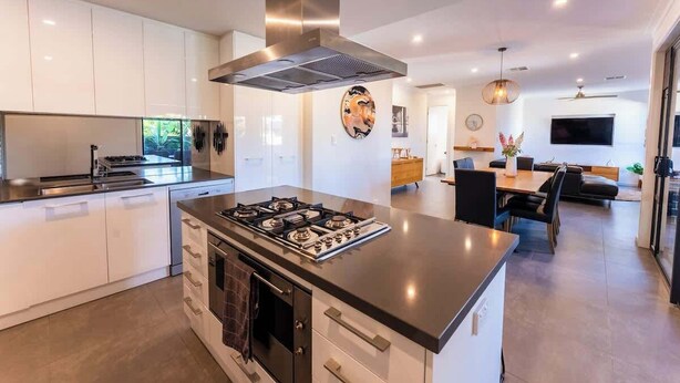 A modern kitchen with a central island, built-in appliances, and a dining area with a TV. - Grange Retreat - Beach, BBQ (Grange)