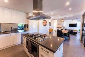 A modern kitchen with a central island, built-in appliances, and a dining area with a TV. - Grange Retreat - Beach, BBQ (Grange)