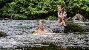 Un hombre y un niño en un río rodeado de densa vegetación verde.