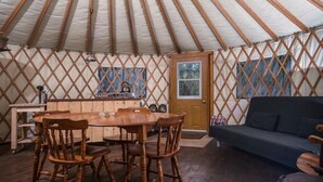 Interior de una yurta con una mesa de madera en el centro, cuatro sillas, un sofá y una claraboya circular.
