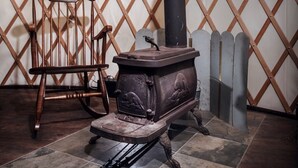 Un horno de madera tradicional con chimenea, una mecedora y un muro ajado en una estructura similar a una tienda de campaña.