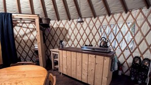 Un ambiente acogedor con una mesa de madera y un banco, una pequeña zona de cocina con un hervidor y un armario de almacenamiento.