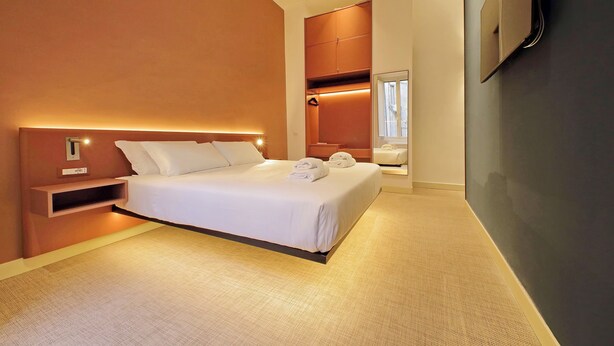 A modern hotel room with a large bed, built-in wardrobe, and a flat-screen TV mounted on the wall. - Velvet Inn (Rome)