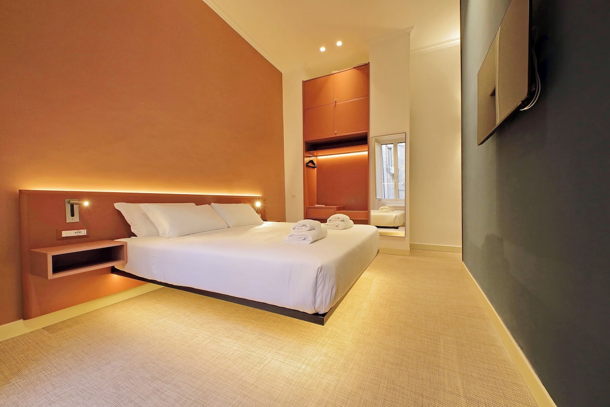 A modern hotel room with a large bed, built-in wardrobe, and a flat-screen TV mounted on the wall.