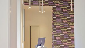 A reception desk with a laptop, a white door in the background, and patterned wallpaper. - Velvet Inn (Rome)