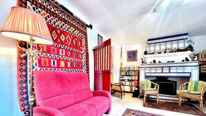 A cozy living room with a red sofa, a patterned wall hanging, a fireplace, and a bookshelf.