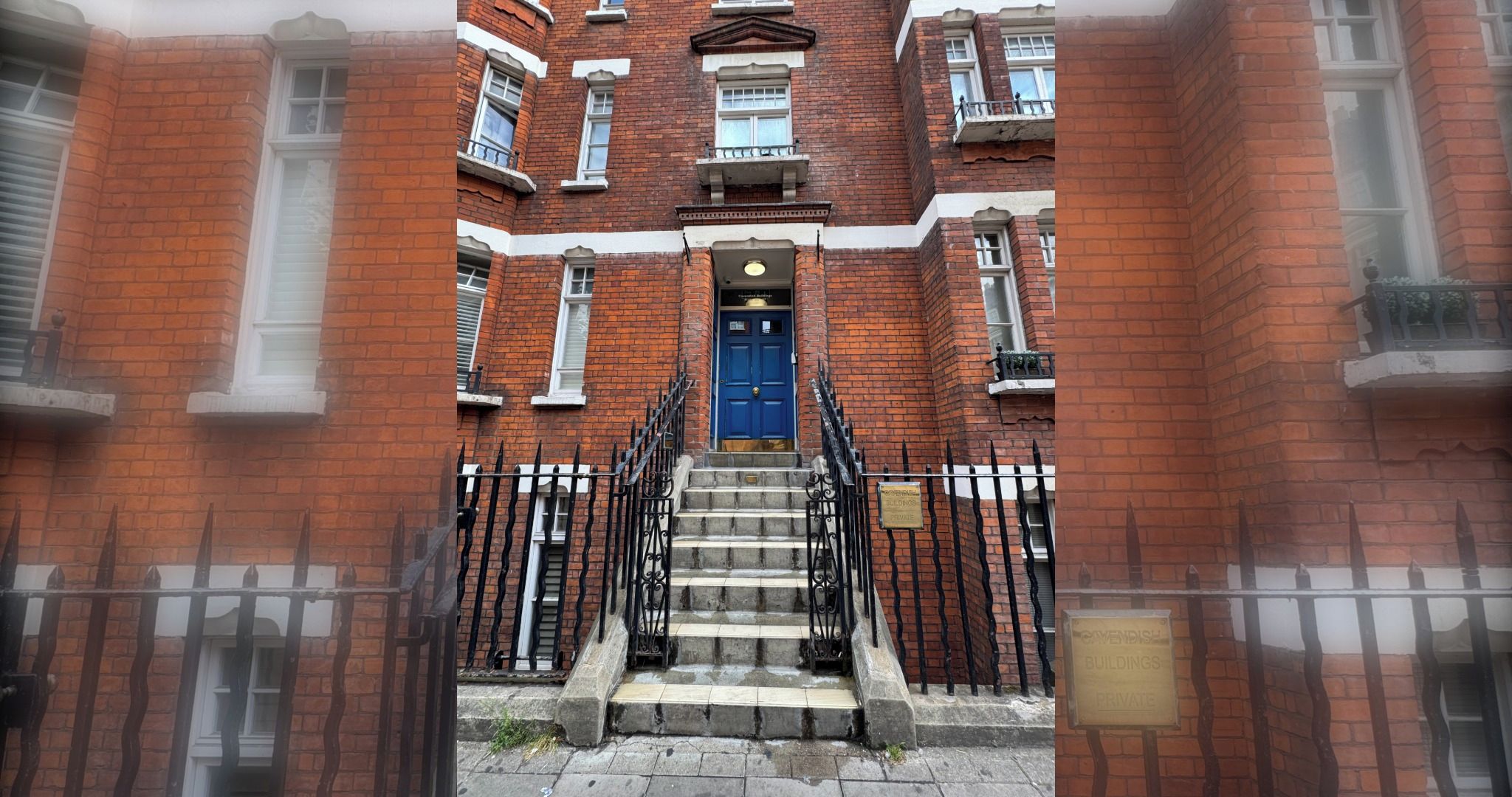 A multi-story brick building with a blue door and a staircase leading to the entrance.